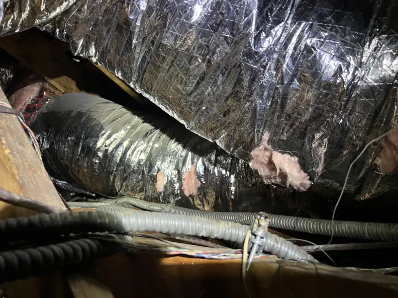 Old ductwork and worn insulation in an attic before removal
